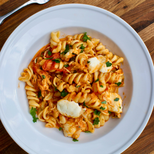 a bowl of corkscrew pasta with tomatoes, basil, chicken, and cheese